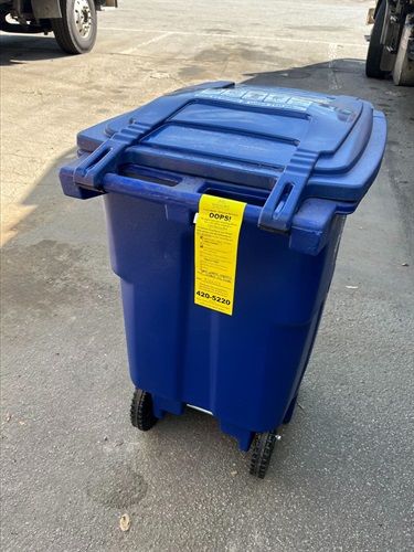 Blue recycling cart with a yellow OOPs tag on the handle