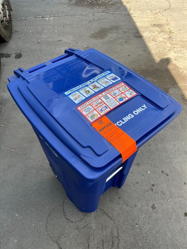 Blue recycling cart with an orange Contamination sticker on the front of the lid.